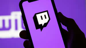 手拿著手機，紫色屏幕上顯示 Twitch 標誌，後面有模糊的 Twitch 標誌。