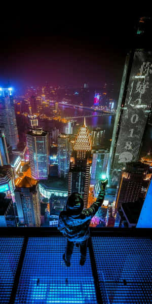 玻璃露台上的人俯瞰夜晚發光的城市 — Pixel 3 壁紙
