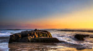 海洋上的夕陽，海浪拍打海灘上長滿苔蘚的岩石