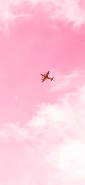 一架飛機在粉紅色的天空背景下飛行，伴隨著蓬鬆的白雲。