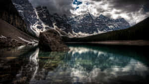 平靜湖中的一塊大石頭倒映著白雪覆蓋的山脈和暴風雲。