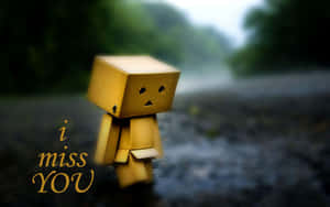 一個黃色紙箱角色站在雨中，旁邊有發光的「i miss YOU」文字。