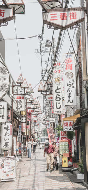 行人沿著一條狹窄的日本街道行走，街道兩旁掛滿色彩繽紛的招牌。
