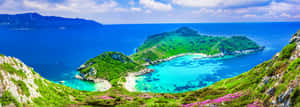 一個令人驚嘆的碧綠色海灣，被綠色島嶼和岩石峭壁環繞，點綴著粉紅色的花朵。 — 超寬螢幕 壁紙