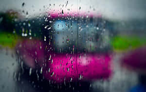 車窗上的雨滴，背景是模糊的粉紅色和綠色城市燈光。