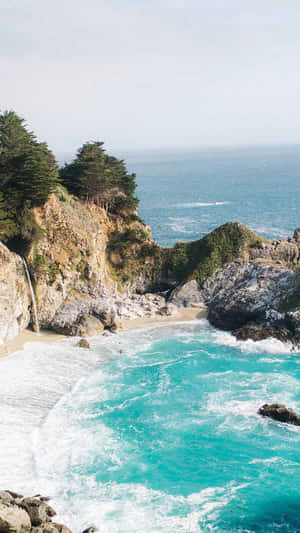 碧綠色的海浪在樹木成蔭的懸崖下的岩石海灘上拍打。