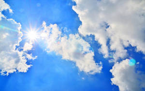太陽穿過白雲，在清澈的藍天中閃耀，帶有鏡頭光暈。