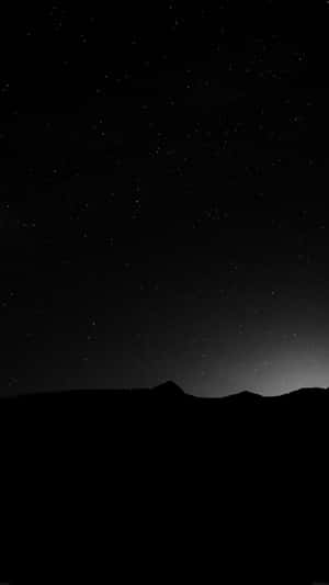 在星空夜空下，帶有柔和暮色光芒的山脈輪廓。 — 黑色 iPhone 壁紙