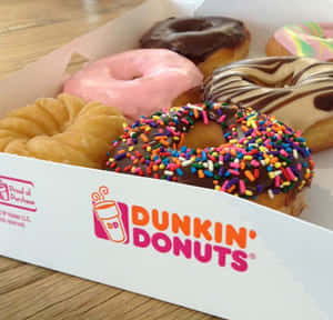 一個裝滿各種彩色灑糖粒和糖霜的Dunkin' Donuts盒子放在木質表面上。