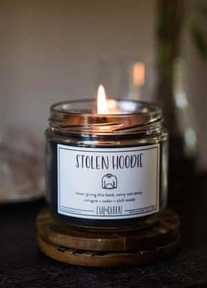 在昏暗房間的木製杯墊上，點燃的蠟燭帶有「STOLEN HOODIE」標籤。
