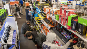 Shoppers browse gaming gear and electronics in a busy retail store aisle.