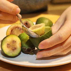 雙手用湯匙在碟上舀取菲油果。 — 銀色 壁紙
