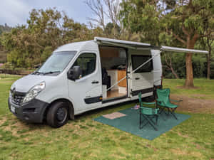 白色露營車停在草地，側門打開，綠色露營椅。