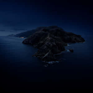 在繁星點點的夜空下，海洋中的一個黑暗岩石島嶼，遠處可見燈光。