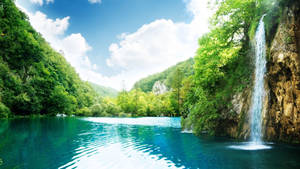 一條瀑布流入一個位於森林山谷中的清澈藍色湖泊，天空晴朗。