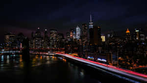 紐約天際線的夜景，建築物燈火通明，橋上的交通燈流動。