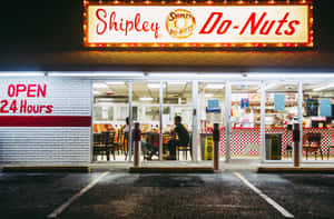 夜間亮燈的24小時Shipley Do-Nuts餐廳，裡面有人坐著。