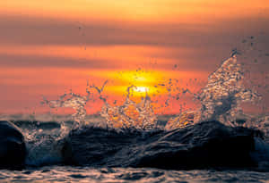 海浪在夕陽下撞擊岩石，帶有鮮豔的橙色和金色光線。