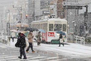 人們撐傘在日本城市中靠近電車的雪地上過馬路。 — 冬日美學 壁紙