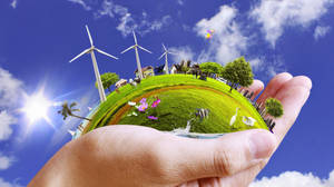 手裡拿著一個小地球，上面有風力發電機、房屋和動物，在陽光明媚的天空下。