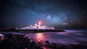 被雪覆蓋的燈塔在繁星點點的夜空下發出紅光，銀河在平靜的海洋上方。