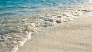 泡沫般的海浪在明亮的陽光下翻滾到金色沙灘上。