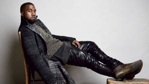 Kanye West 坐在椅子上，身穿質感外套和皮褲。