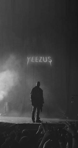 剪影表演者在舞台上，上方有「YEEZUS」標誌，下方群眾伸手向上。