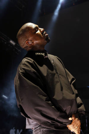 Kanye West 在明亮的聚光燈下雙手合十在舞台上表演。