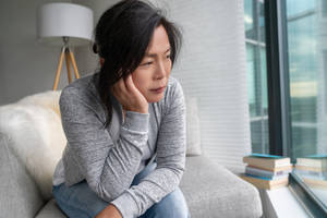 女士坐在沙發上望向窗外，附近有書本