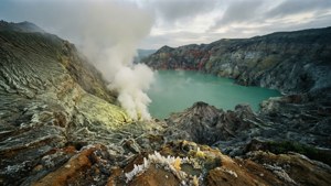 一個火山口湖，湖水呈綠松石色，邊緣升起蒸汽，周圍環繞著崎嶇的岩石 formations。