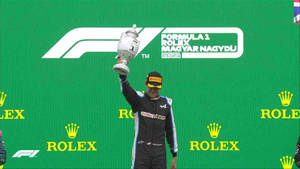F1車手在帶有Rolex標誌的綠色頒獎台上手持獎盃。