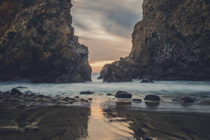 夕陽的光線穿過岩石海灣，帶有霧氣般的海浪和濕沙。