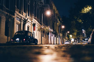 復古汽車停泊在夜間光線昏暗的城市街道上，伴隨著發光的路燈。 — 夜晚 GIF 壁紙