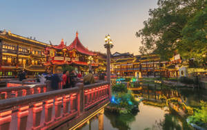 一座紅橋橫跨運河，兩旁是傳統中式建築和發光的燈籠，在黃昏時分。