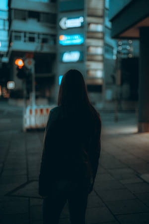 在發光的霓虹燈招牌下，夜晚的城市街道上獨自站立的剪影人物。