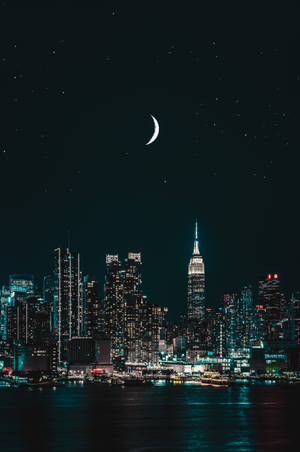 紐約市夜景，天際線上方有月亮和星星，倒映在水中 — 手機 壁紙
