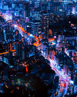 充滿活力的城市夜間鳥瞰圖，有發光的藍色建築物和來自移動車輛的橙色光跡。 — 夜晚 GIF 壁紙