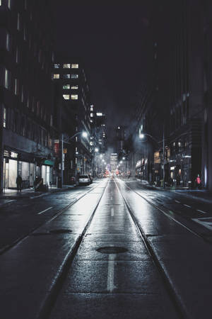 夜晚一條安靜濕漉漉的城市街道，有發光的街燈和建築物窗戶。
