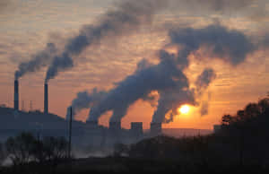 工廠煙囪向發光的橙色夕陽天空排放黑色煙羽。 — 煙霧動畫 壁紙