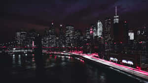 夜間城市天際線，建築物燈火通明，水面上有紅色光跡。