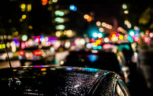 引擎蓋上的雨滴反射出夜晚多彩的城市燈光。 — 夜空 壁紙