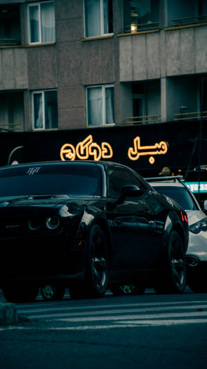 黑色肌肉車停在黃昏的城市中，發光的阿拉伯霓虹燈招牌下。 — Dodge challenger GIF 壁紙