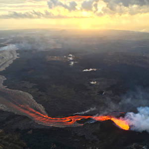 熔岩河流經黑暗的火山景觀，在金色日落天空下。