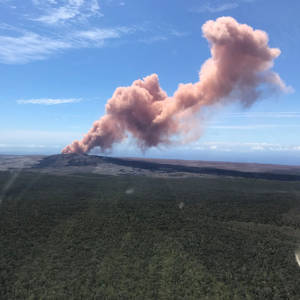 火山爆發，粉紅色灰雲籠罩著綠色森林和藍天。