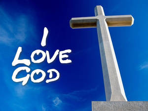 一座石十字架，上面有「I LOVE GOD」文字，背景是清澈的藍天。