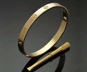 金色Cartier love手鐲與螺絲刀在深色反光表面上。