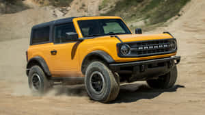 黃色福特Bronco SUV在塵土飛揚的沙漠地形上行駛。