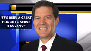 堪薩斯州州長 Sam Brownback 身穿西裝微笑，身後有新聞圖像。 — 政治 壁紙