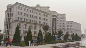 一座帶有拱形窗戶和圓頂的大型白色建築，周圍環繞著樹木和噴泉，廣場上有人們。